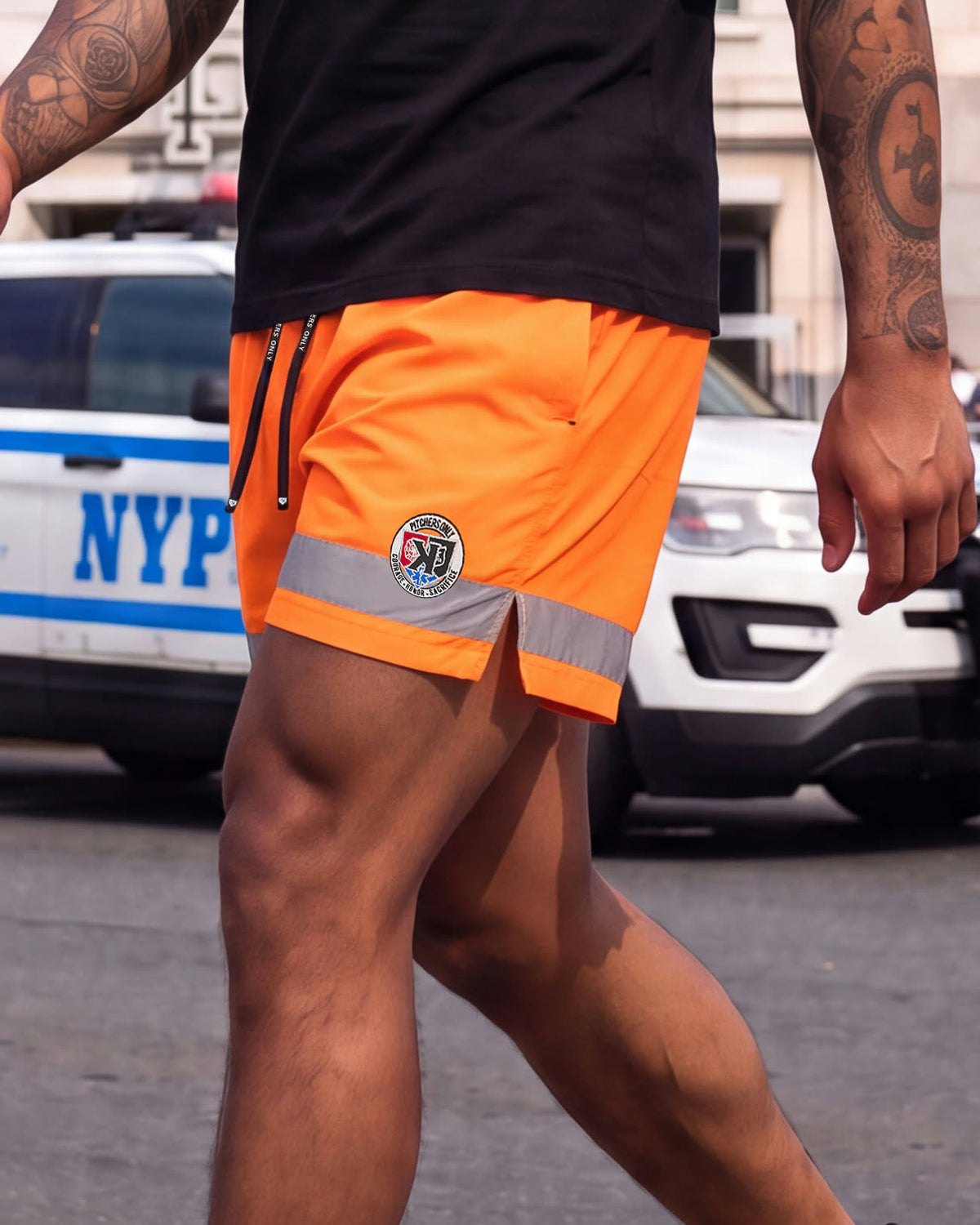 Close-up of the First Responders Shorts patch and 3M reflective trim beside an NYPD cruiser