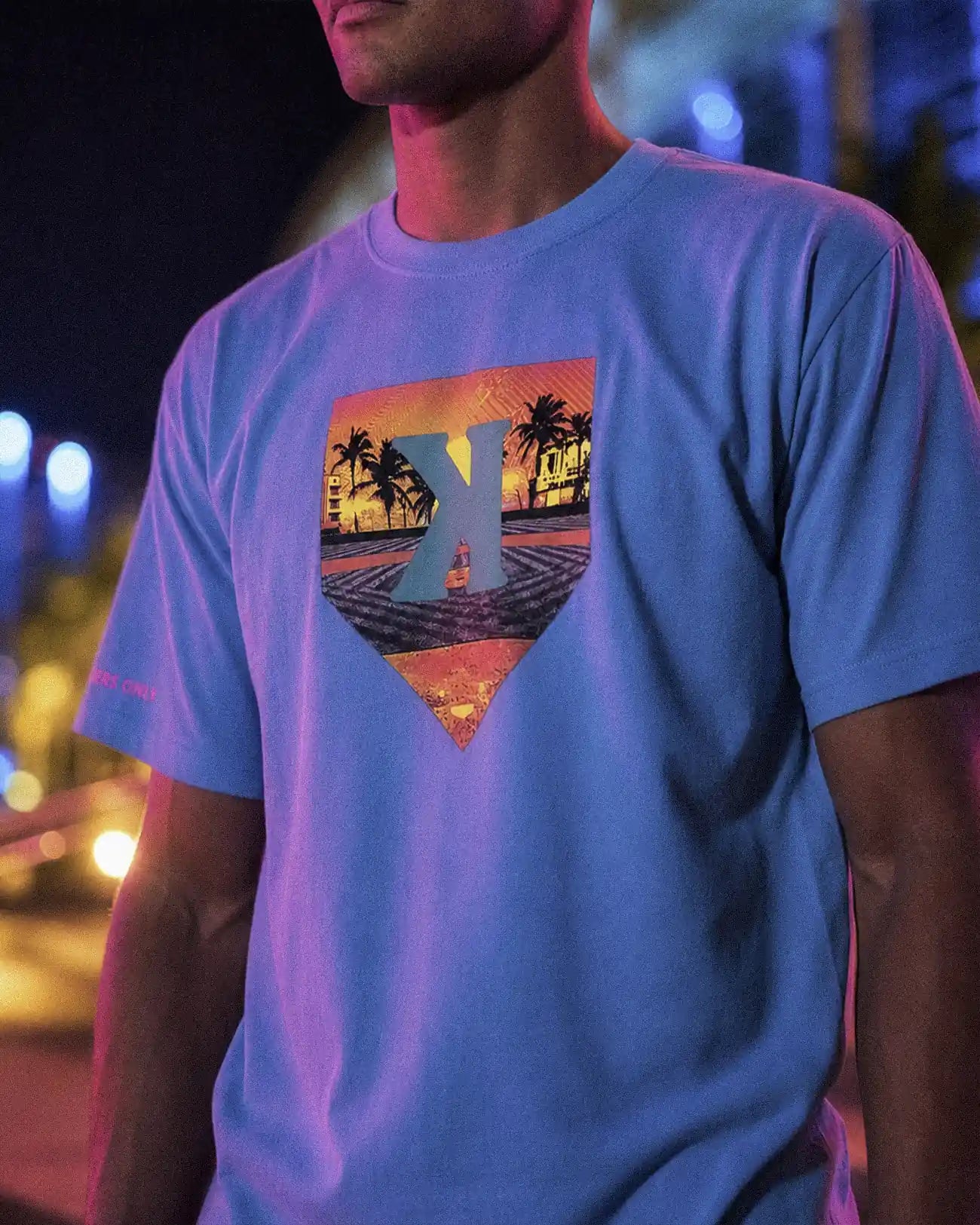 Youth Summer Nights Tee worn at night, sunset home plate K graphic with palm trees on the front