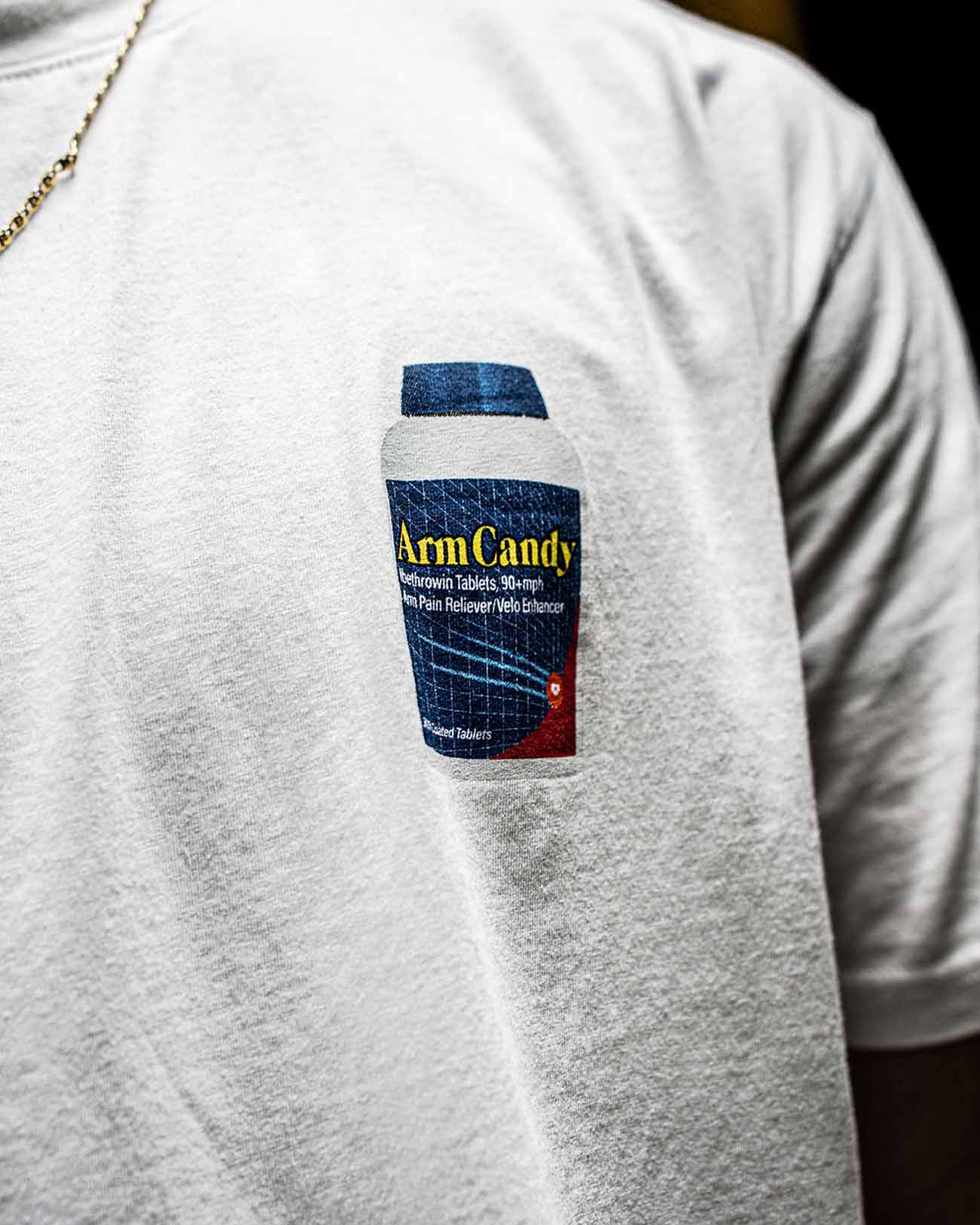 Tight shot of Pitchers Only Arm Candy white t-shirt with Ibethrowin graphic design on baseball player model from front.