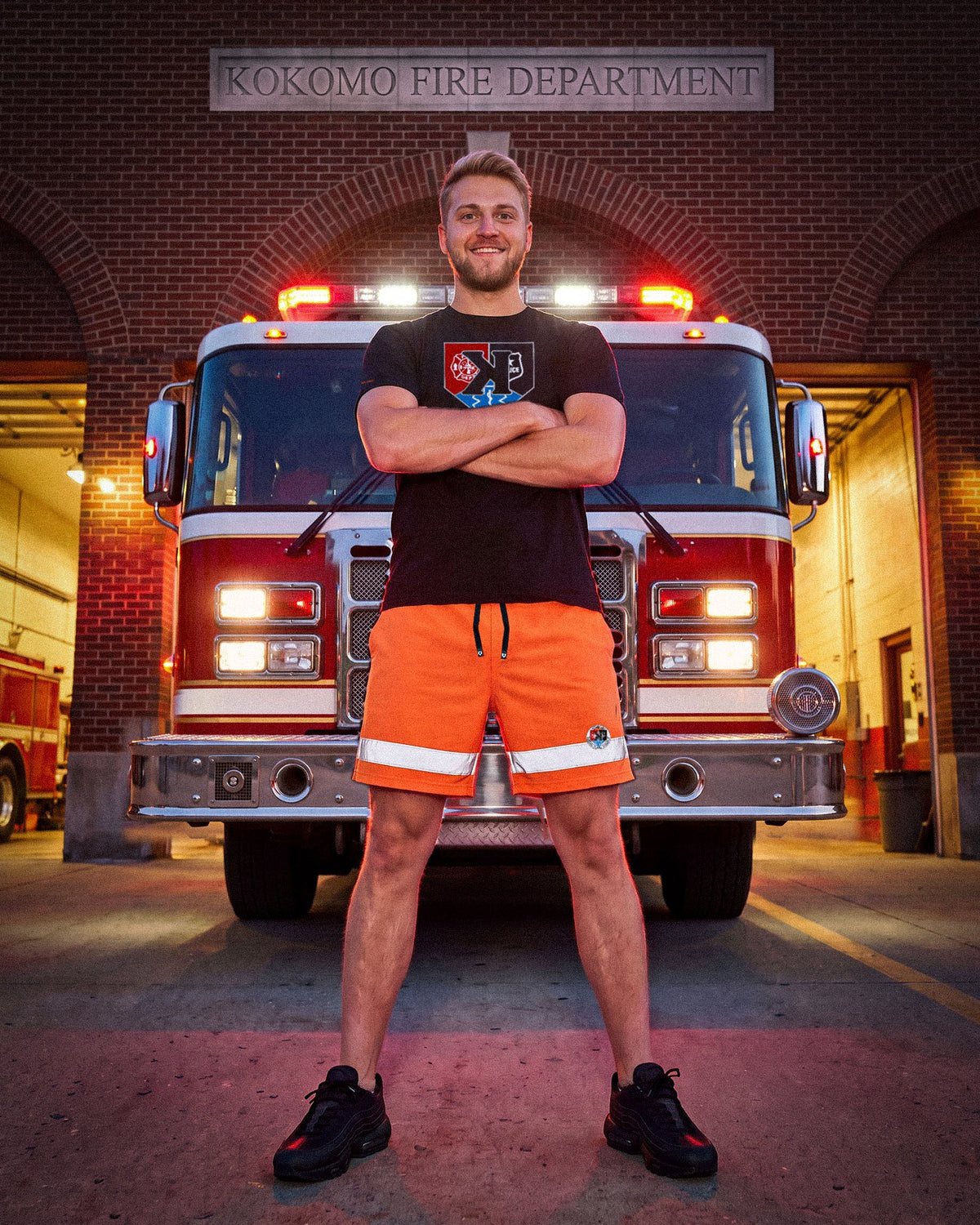 Model in the First Responders Tee and Safety Orange Shorts in front of a fire engine at the Kokomo Fire Department - Pitchers Only