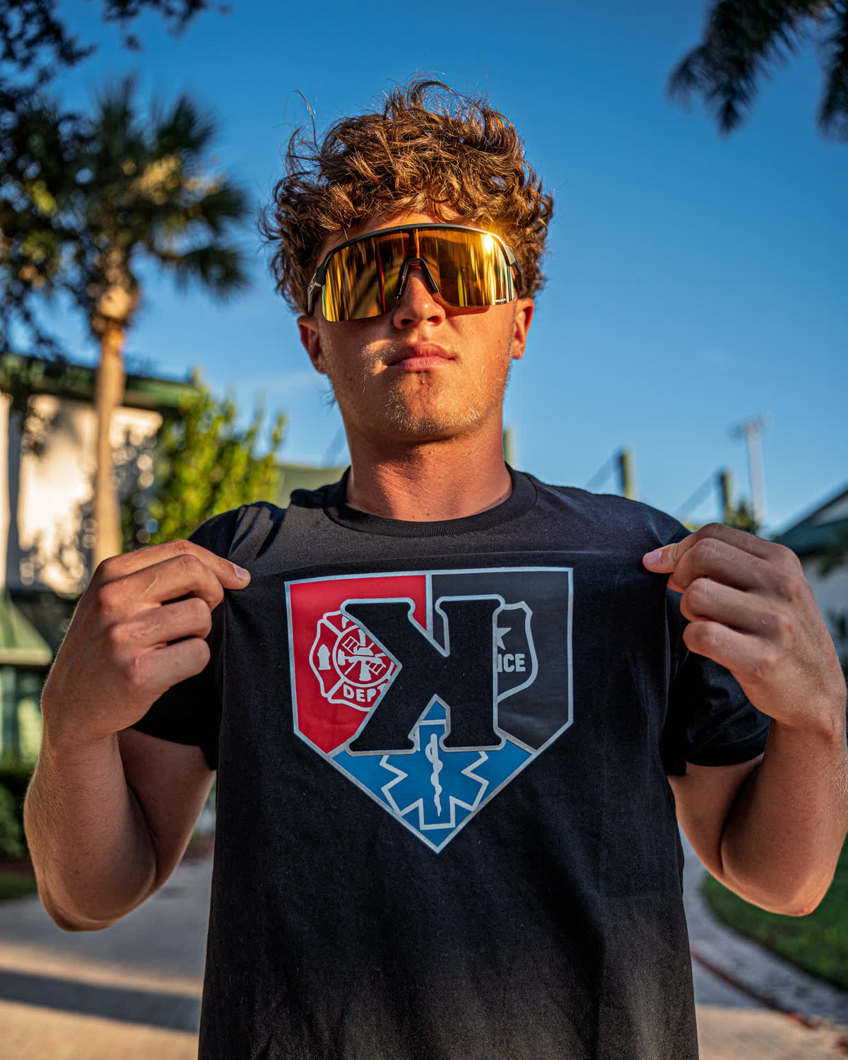 Pitcher holding out the front of the First Responders Tee to show the fire, police and EMS badges on home plate - Pitchers Only