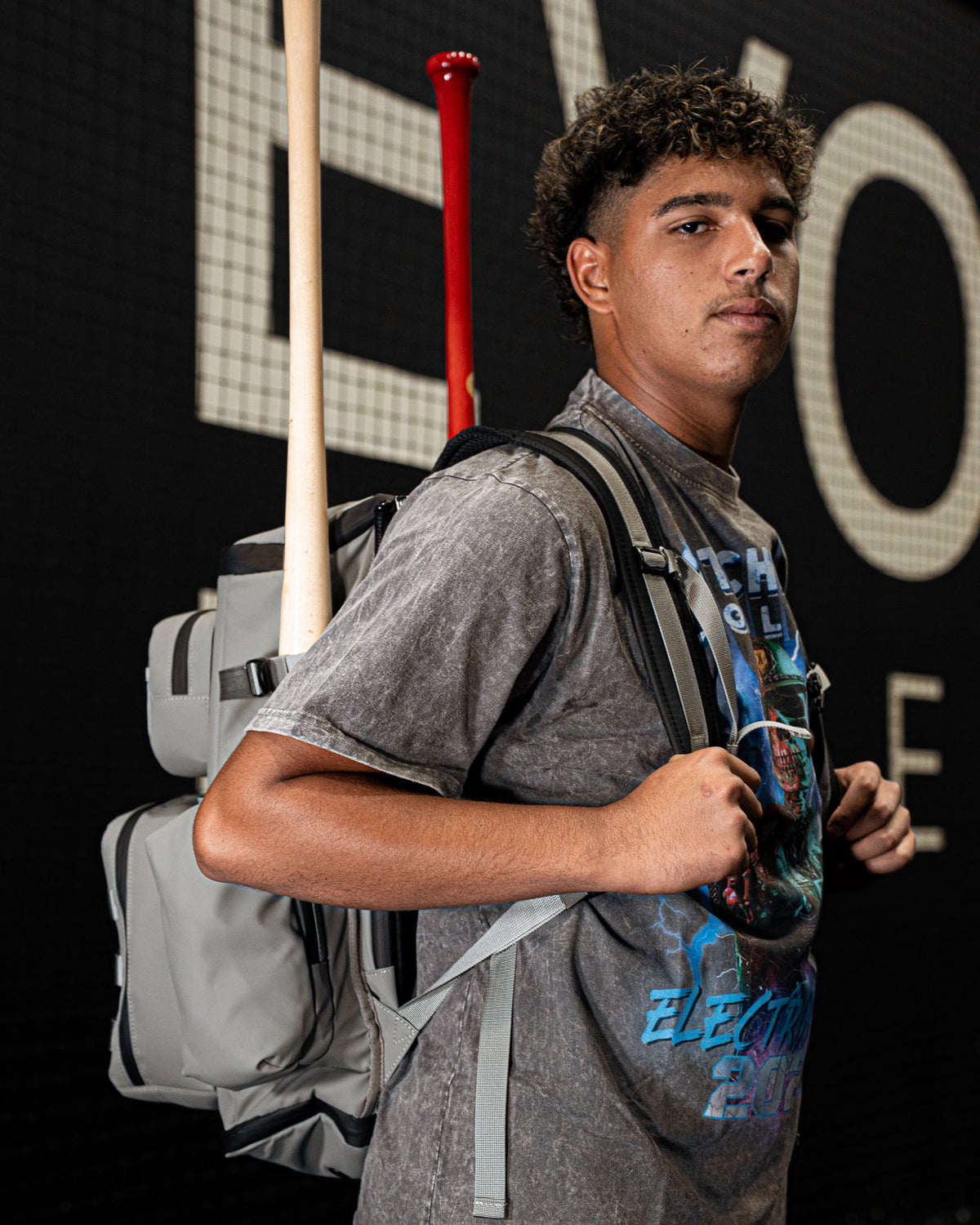 Baseball player wearing the Pitchers Only Wolf Gray Shove Day Bag with bats racked behind him.